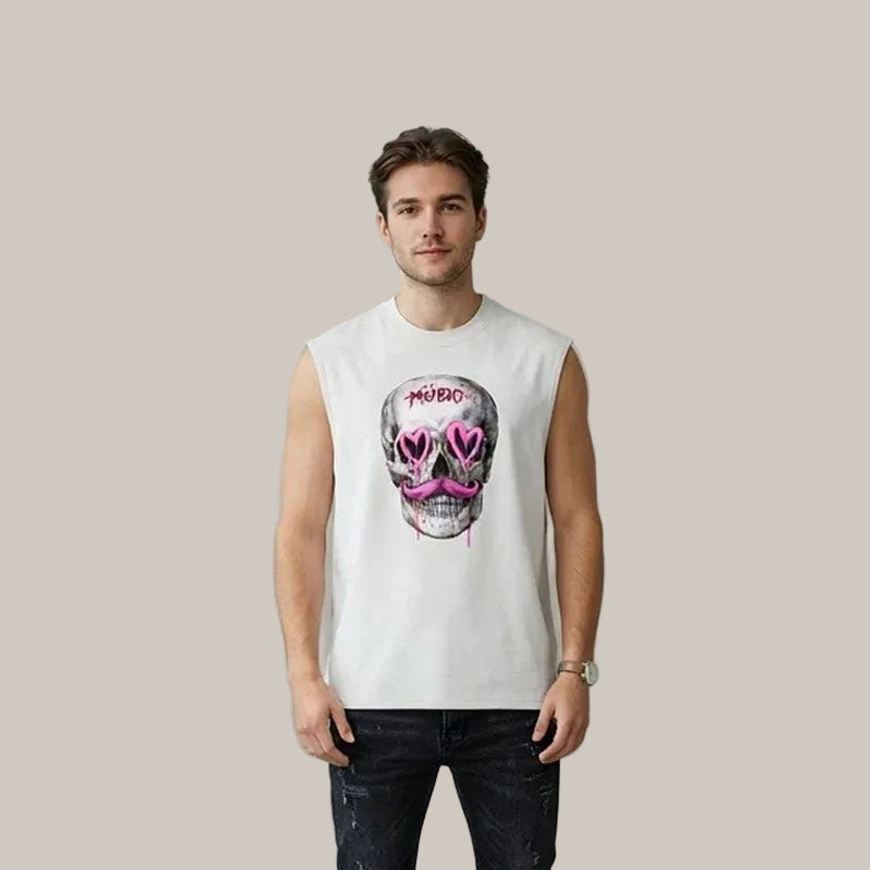 A man wearing a white sleeveless t-shirt with a graphic of a skull wearing pink heart-shaped sunglasses and the word 'MURDER' above it, paired with dark jeans, standing against a textured gray wall.