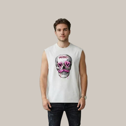A man wearing a white sleeveless t-shirt with a graphic of a skull wearing pink heart-shaped sunglasses and the word 'MURDER' above it, paired with dark jeans, standing against a textured gray wall.