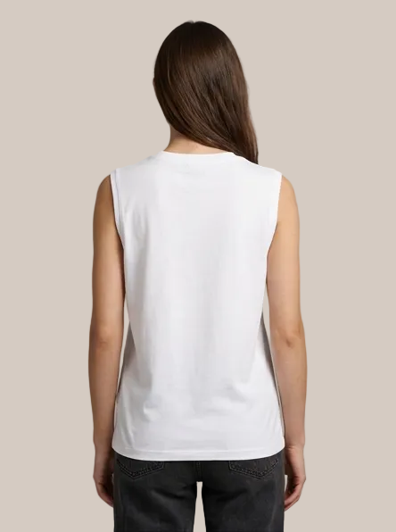 A woman viewed from the back wearing a plain white sleeveless top and dark gray jeans, standing against a solid light gray studio background.