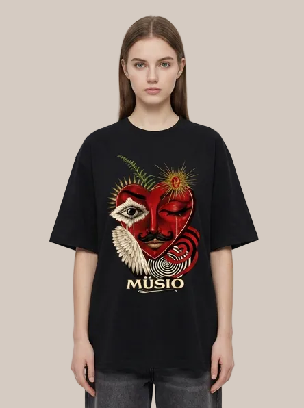 A model wearing a black oversized t-shirt with a large graphic print on the front. The graphic features a stylized red heart, a white eye with a feather, a mustache, a sun, and the word 'MÚSIO' printed below in gold.