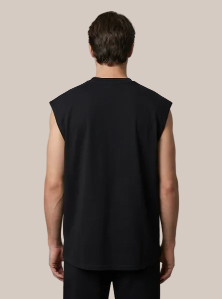 A man viewed from the back wearing a black sleeveless t-shirt and black pants against a plain gray studio background.