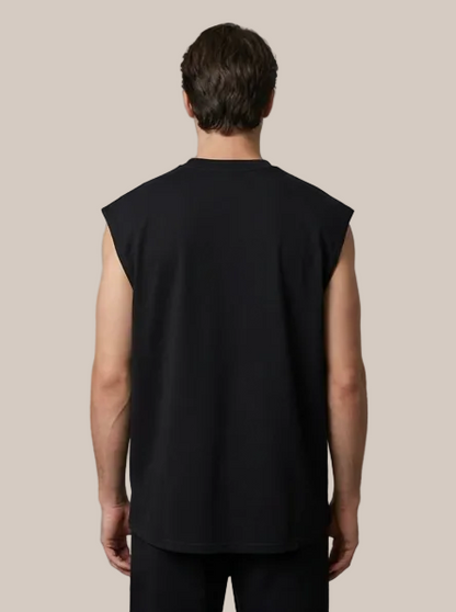 A man viewed from the back wearing a black sleeveless t-shirt and black pants against a plain gray studio background.