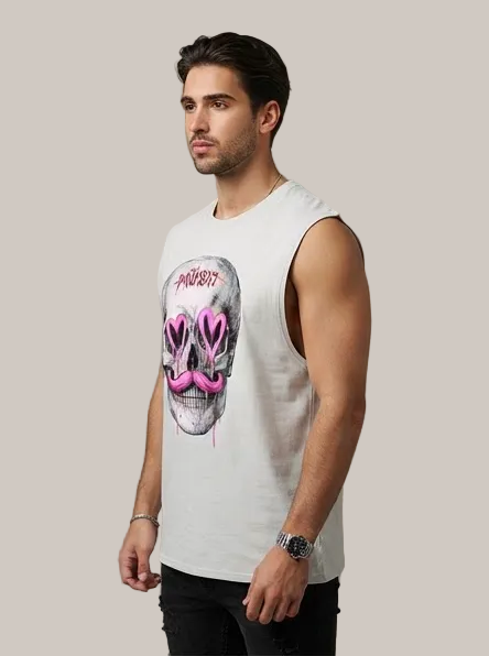 A man wearing a sleeveless white tank top with a large skull graphic featuring pink heart-shaped eyes and the word 'PROHIBIT' above it, paired with black pants, standing against a textured gray wall.